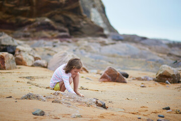 Adorable preschooler girl playing on the beach at Atlantic coast of Brittany, France