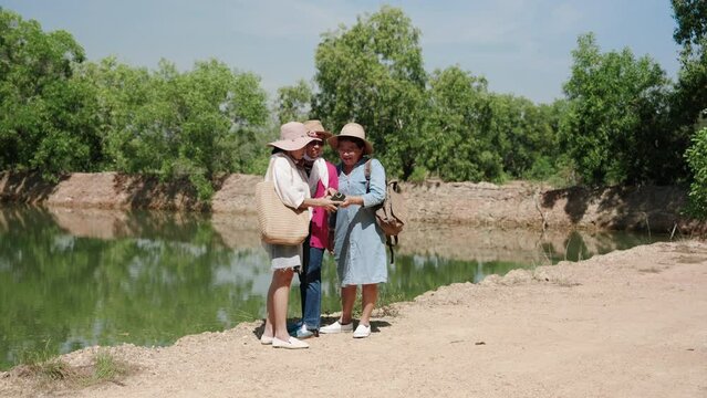 Three Asian women best friends, come travel nature, relaxing, together after retirement, using pension money, stand by water admire atmosphere, beautiful natural views, opening map see direction.