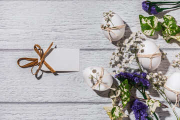 White Easter eggs with sprigs of gypsophila and a greeting label on a white wooden background....