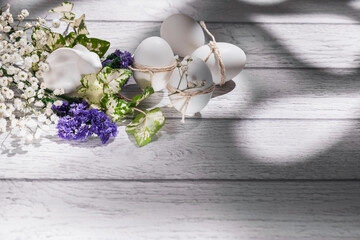 White Easter eggs with sprigs of gypsophila, white Easter bunny on a white wooden background....