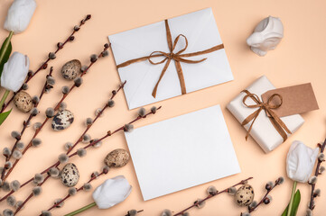 Gift white box and envelope on a peach background with willow branches and white tulips, Easter...