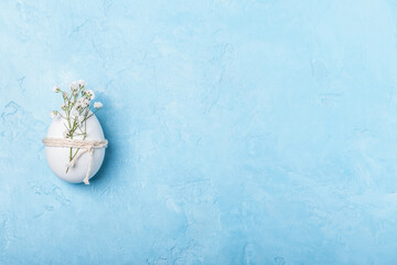 White Easter egg tied with twine with a sprig of gypsophila on a blue background. Easter...