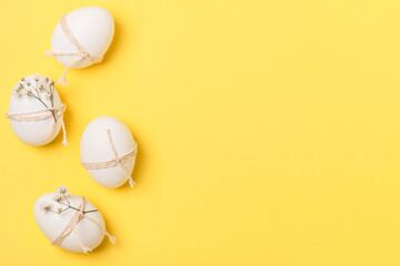 White Easter eggs decorated with twine and sprigs of gypsophila on a yellow background. Easter...