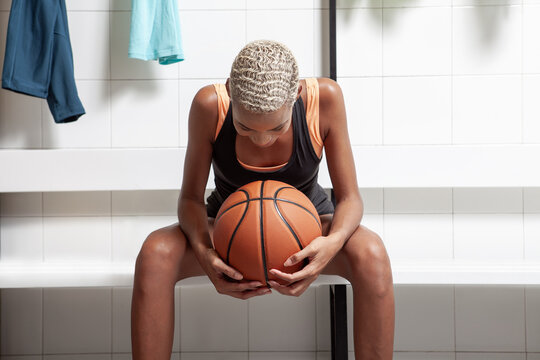 Sport basketball player in the locker room, a African American female athlete holding the ball before the game, competition or training. Woman sitting in changing room with basket ball