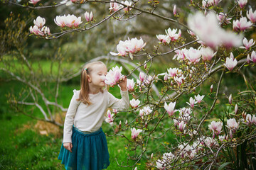 Adorable preschooler girl enjoying nice spring day in park during magnolia blooming season