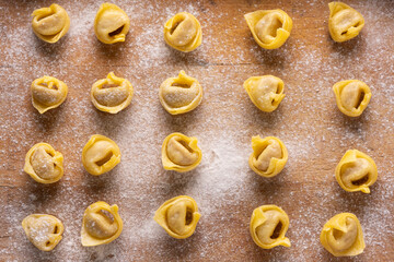 in the foreground, seen from above, raw tortellini Bolognese style on a floured wooden board - 724834960