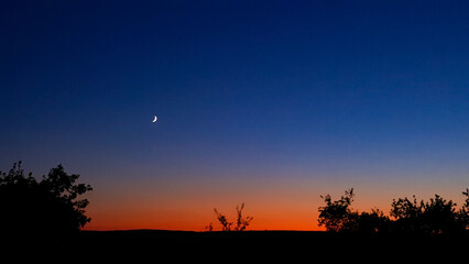 Young crescent moon on a clear sky at the end of the day in the summer