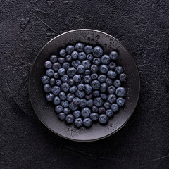 from above, on a black textured background, a black plate with fresh wet blueberries.