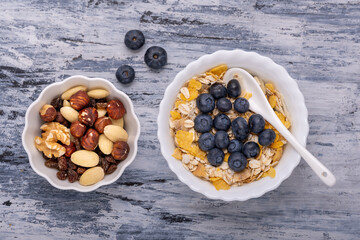 from above, on a structured background, the ingredients for a healthy breakfast with wholemeal and organic oat flakes, cereals, dehydrated fruit, dried fruit and fresh blueberries.