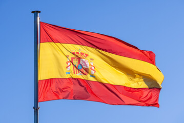 Spanish flag waves in the wind against a blue sky, banner blowing like soft silk
