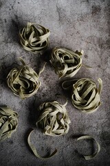 Dry raw spinach fettuccine pasta on rustic background, selective focus
