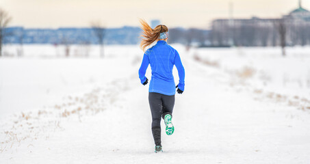 Female runner jogging in cold winter forest wearing warm sporty running clothing