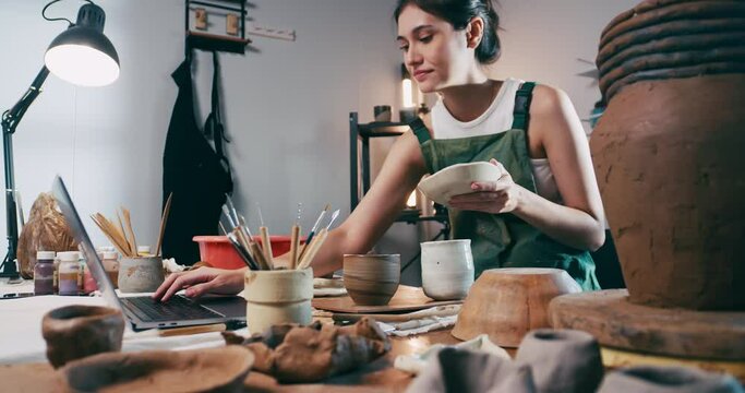 A young female ceramicist is checking ceramic orders for customers. Asian woman is enjoying pottery work.