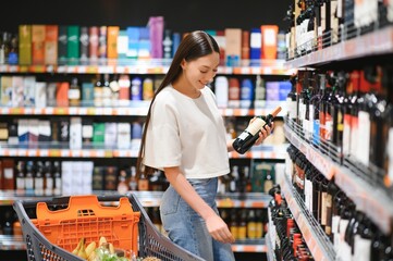 Young woman deciding what wine to buy in supermarket