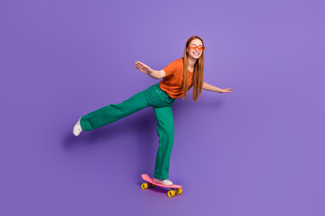 Photo of positive lovely happy girl teenager wearing stylish clothes standing penny board isolated on purple color background