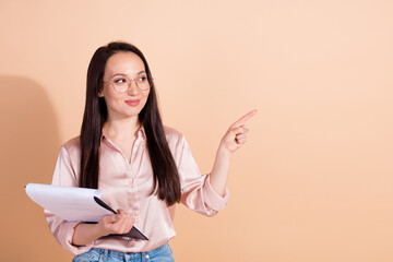 Portrait of smart woman dressed silk blouse in eyewear hold clipboard look directing empty space isolated on beige color background