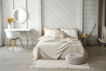 Scandi bedroom interior, a bed with pillows and a blanket in beige colors, a white table with a...