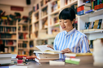 A smiling Asian female spends the afternoon at the library, reading a book.