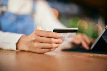 Close-up photo of a female holding and using a credit card, entering data into the tablet.