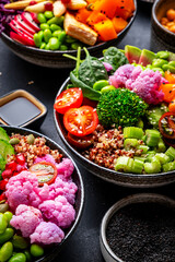 Vegan buddha bowls set with pumpkin, quinoa, tomatoes, spinach, avocado, radish, soybeans, tofu, cabbage and seeds on black table background, top view. Healthy menu, vegetarian comfort food
