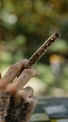 a tattooed hand holding a marijuana blunt in outdoor park