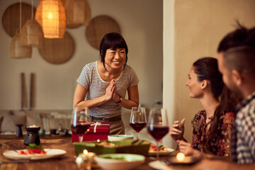 A thankful Asian woman having dinner with her friends, at home.