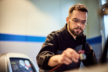 A focused mechanic, doing his job, filling the air conditioner in the car.