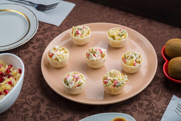 on the table is a salad in tartlets in a plate on a brown tablecloth.