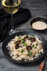 Risotto with mushrooms, parsley, parmesan and a glass of white wine on a dark background.