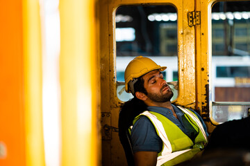A male worker lies down on a stretch chair taking a midday nap during his break. A tired male worker rests in the work area.