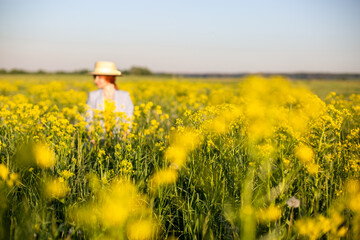girl in an out-of-focus hat on a blooming yellow rapeseed field.