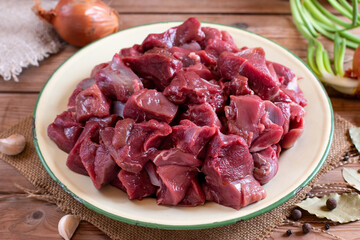Raw fresh beef or lamb cubes. Diced red beef meat on a wood serving board. Raw casserole or stewing beef diced. Goulash.