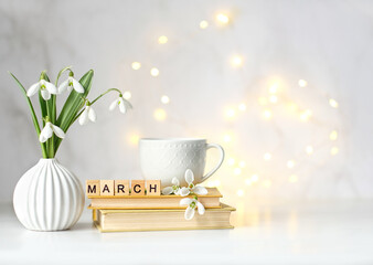 Bouquet of snowdrop flowers, cup, books and wooden letters 