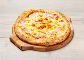Pizza with ham, pineapples and cheese on a wooden board