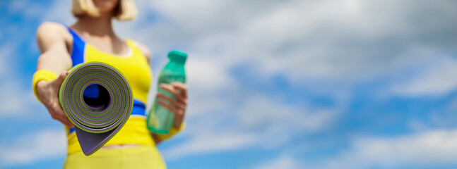 Woman in sports wear is holding a yoga mat and a bottle of water. Yoga mat and water bottle. Healthy lifestyle concept