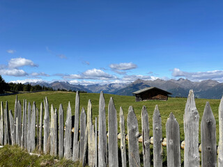typical wooden fence of Rodenecker alm in northern Italy with a wooden cabin and the Dolomiti mountains in the distance