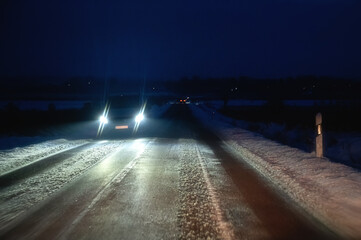 Licht vom Gegenverkehr blendet auf eisiger Fahrbahn im Winter bei Nacht