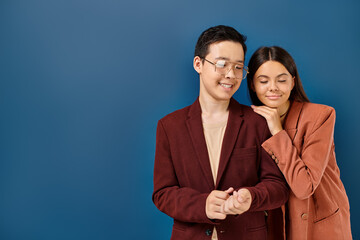 cheerful elegant diverse teenagers in fashionable blazers posing together on dark blue backdrop