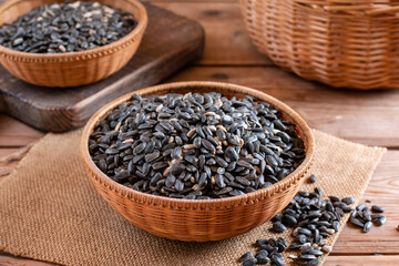 Black sunflower seeds in small brown wooden cup, on wooden table