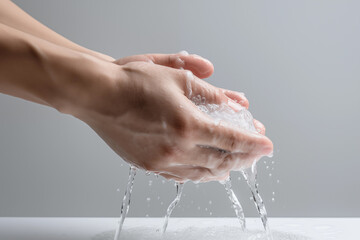 Woman washing her hands with water on gray background, closeup of hands