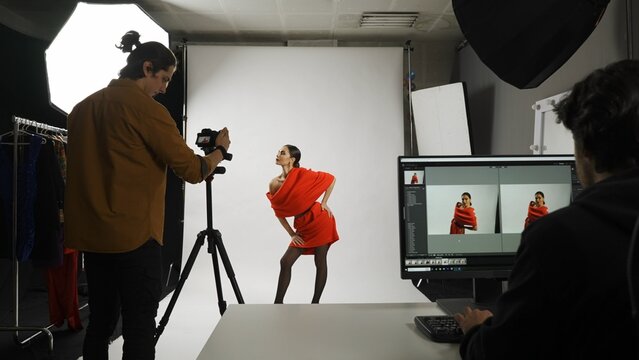 Backstage of model and professional team in the studio. Appealing woman posing for photographer, male editor looking at monitor checking photos.