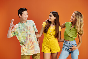 joyous multicultural teenagers in vivid casual outfits looking at each other on orange backdrop