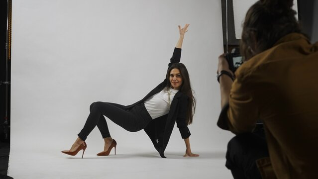 Backstage of model and professional team in the studio. Full length of attractive model in suit posing on the floor, photographer taking photos.