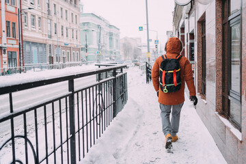A man walks through the snow-covered streets of the city. The man is wearing gray trousers, an...