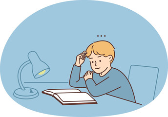 Little boy child sit at table at home studying with textbook under lamp. Smart kid enjoy reading at desk. Education and literature.