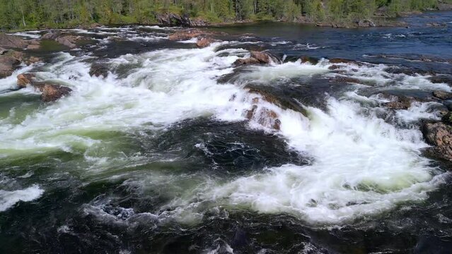 Soaring low, the drone footage reveals the turbulent beauty of Namsskogan's Namsen River, etching a wild path through the lush Norwegian landscape (drone flies smoothly and low along the cascades)