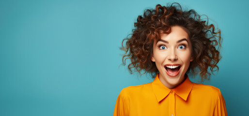 A young woman on a blue background with space for text, overjoyed by information or an attractive offer, laughs at the viewer.