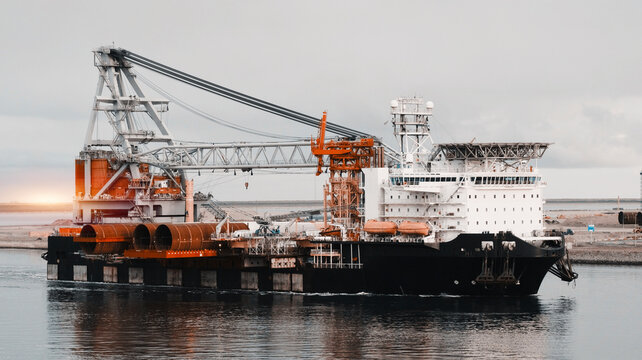 Wind Generators And Offshore Construction Crane Vessel With The Cargo Of Monopiles On Deck. Ship With Motion Compensated Pile Gripper And 8-point Anchor Mooring System