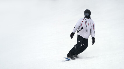 A lone snowboarder wearing a protective helmet rolls down a snowy ski slope. Copy space.