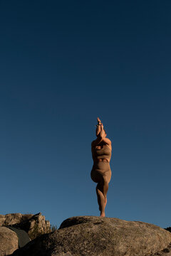 Flexible woman practicing garudasana yoga on rocky cliff